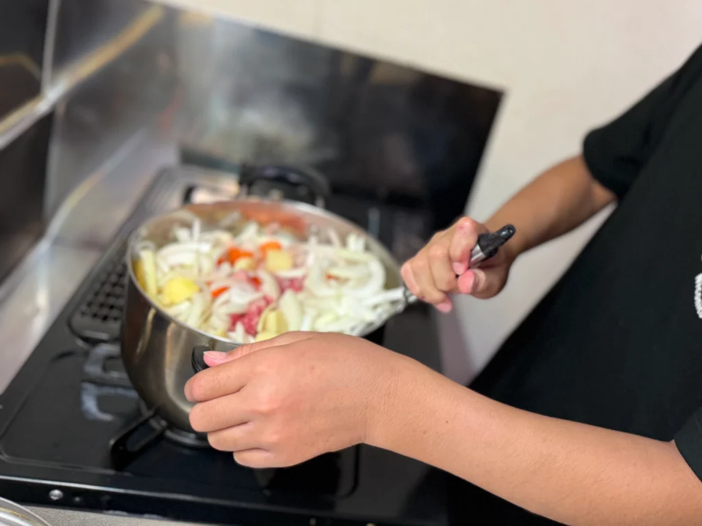 森のコテージでカレーの具材を炒める子ども