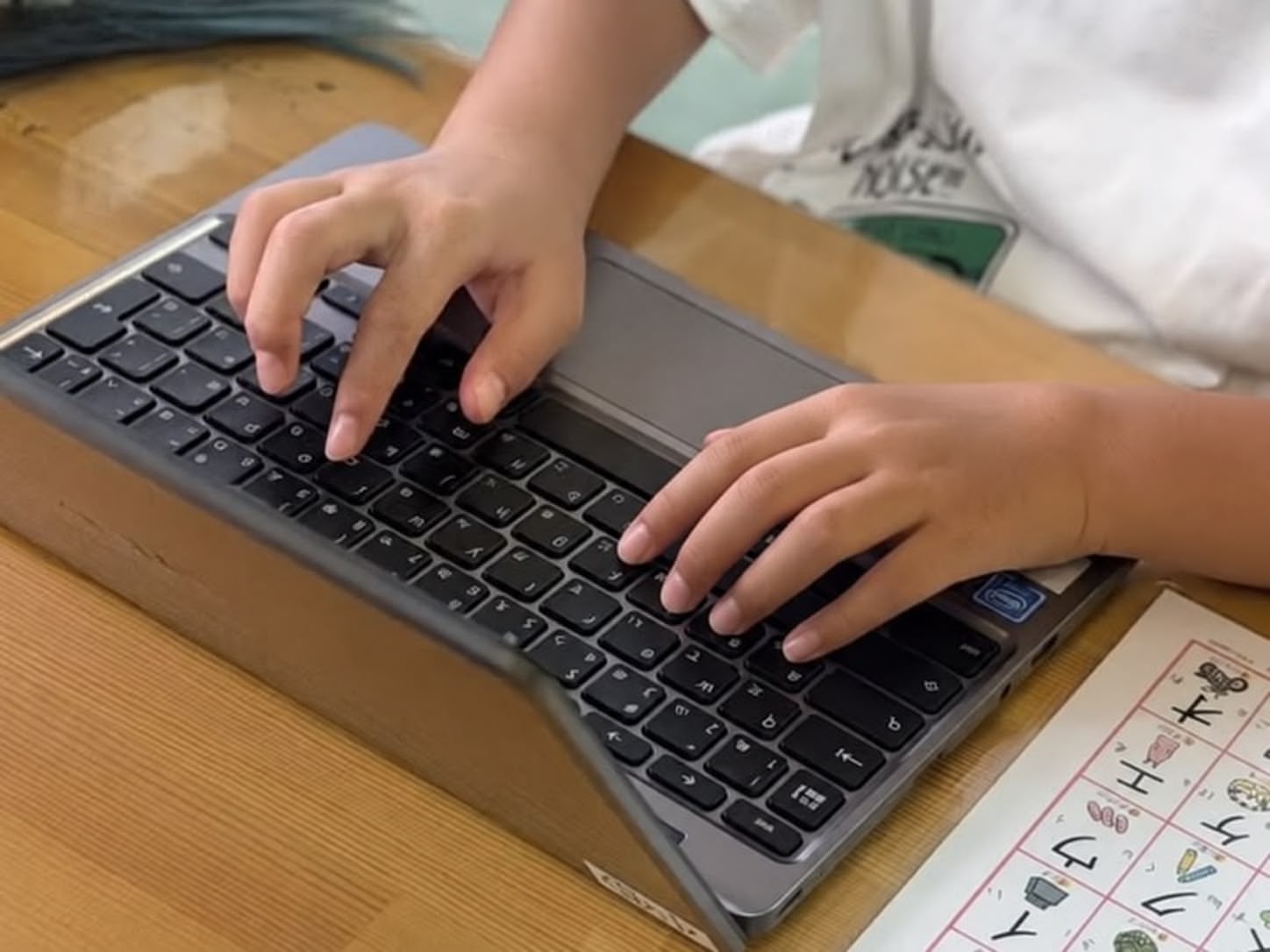ノートパソコンのキーボードで文字を入力する子どもの手元