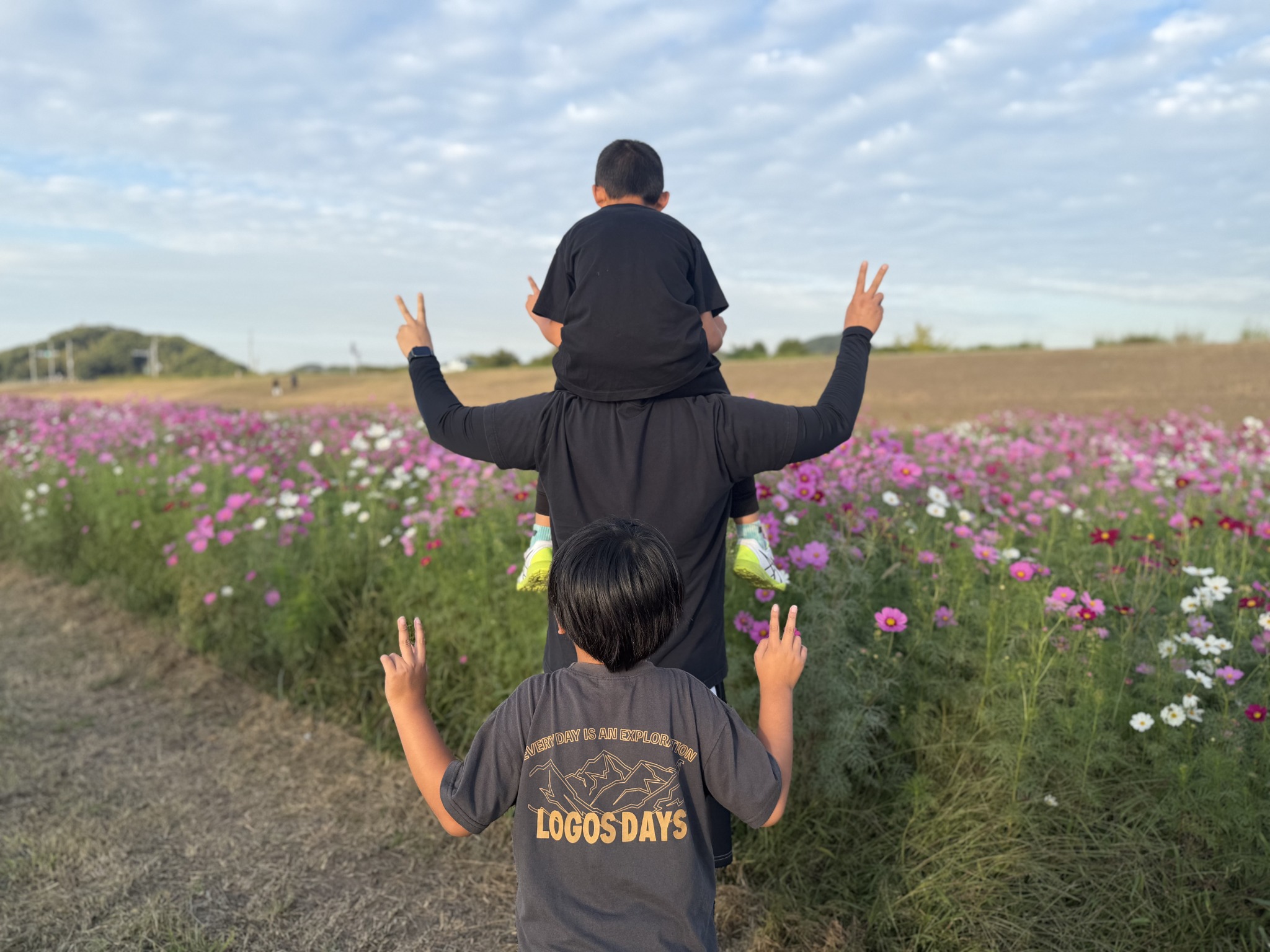 コスモスを背景に後ろ姿でピースをする子どもたち