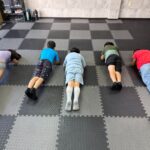 マットの上に並び、肘とつま先で体を支える運動に取り組む子どもたち
